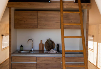 Interno di tenda safari con cucinotto moderno, scala di legno e letto soppalcato sopra i mobili.