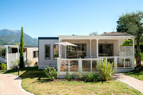 Exterior view of Cottage Next XL superior lodge with wooden deck, garden plants, and mountain backdrop.