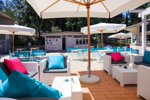 Coin salon extérieur du Vallicella Glamping Resort en Toscane, avec parasols, chaises bleues et coussins colorés.