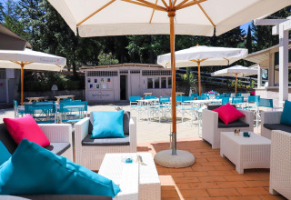 Coin salon extérieur du Vallicella Glamping Resort en Toscane, avec parasols, chaises bleues et coussins colorés.