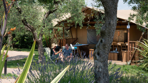 Due persone si rilassano davanti a una tenda safari chiamata Spotty Lodge, circondata dal verde.