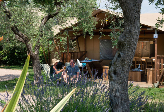 Due persone si rilassano davanti a una tenda safari chiamata Spotty Lodge, circondata dal verde.