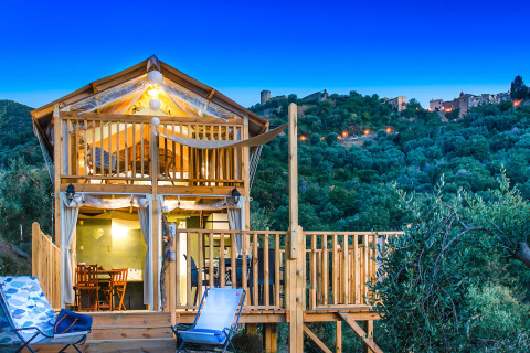 Cabane en bois au crépuscule au Vallicella Glamping Resort en Toscane, Italie, avec collines et village en arrière-plan.
