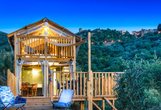 Cabane en bois au crépuscule au Vallicella Glamping Resort en Toscane, Italie, avec collines et village en arrière-plan.