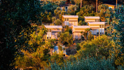 Tentes de luxe au Vallicella Glamping Resort en Toscane, entourées d’arbres sous la lumière du soir.