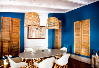 Salle à manger avec chaises blanches modernes, murs bleus, volets en bois et suspensions tressées au Vallicella Glamping Resort.