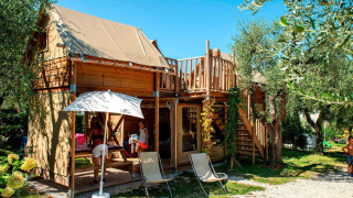 Safari tent with a wooden frame, rooftop terrace, and people enjoying a sunny day outdoors in nature.