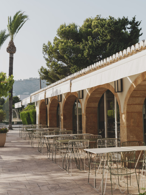 Buitenterras bij Wecamp Jávea in Valencia, Spanje, met metalen tafels, stoelen, bogen en witte zonneschermen.