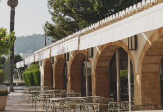 Buitenterras bij Wecamp Jávea in Valencia, Spanje, met metalen tafels, stoelen, bogen en witte zonneschermen.