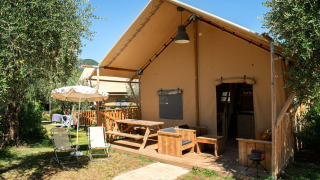 Safari Lodge safaritelte med træterrasse, havemøbler og parasol i et grønt udendørs område.