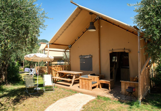 Safari Lodge safaritelte med træterrasse, havemøbler og parasol i et grønt udendørs område.