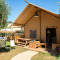 Safari Lodge safaritent met houten terras, picknicktafel, tuinstoelen en parasol in groene omgeving.