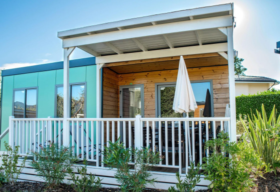 Exterior view of the Next L Deluxe lodge with covered porch, white railing, and lush greenery in front.