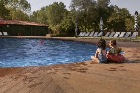Twee kinderen zitten bij het zwembad van Wecamp Santa Cristina in Catalonië, Spanje, met ligstoelen rondom.