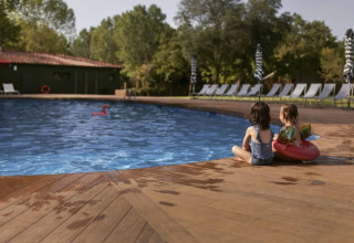 To børn sidder ved poolen i Wecamp Santa Cristina, et feriested i Catalonien, Spanien, omgivet af liggestole.