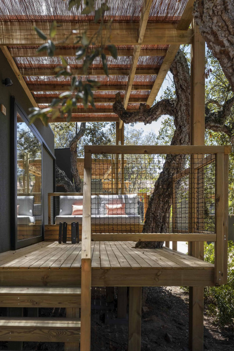 Holzterrasse mit Überdachung und Bänken, integriert in Bäume im Wecamp Santa Cristina, Katalonien, Spanien.