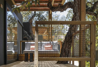Overdekt houten terras met zitbanken en bomen geïntegreerd bij Wecamp Santa Cristina in Catalonië, Spanje.