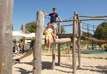 Bambini giocano su una struttura in legno con sabbia in un’area giochi presso un glamping.
