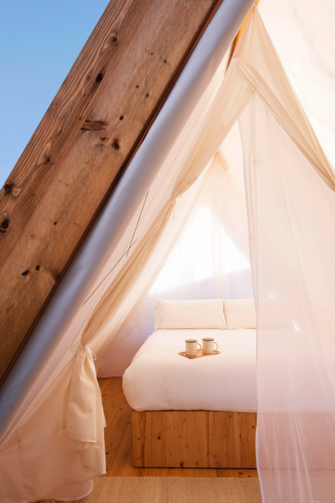 Interior view of a cozy glamping tent with a double bed and mugs at Wecamp Santa Cristina, Catalonia, Spain.