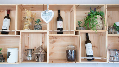 Træhylder med vinflasker, planter, fuglehus og krukker, fotograferet på Chianti Glamping Resort i Toscana.