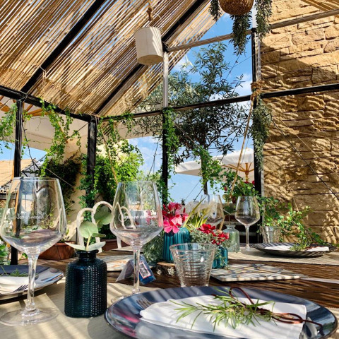 Gedekte tafel met wijnglazen en planten onder een glazen dak bij Chianti Glamping Resort in Toscane, Italië.