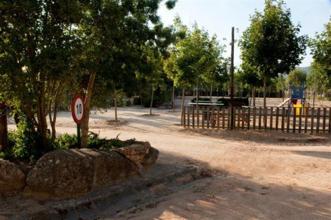 Spielplatz im Wecamp Santa Cristina Ferienpark in Katalonien, Spanien, mit Bäumen, Zaun und Verkehrsschild.
