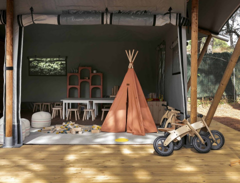 Area giochi per bambini con tenda tipi, biciclette di legno e giocattoli a Wecamp Santa Cristina in Catalogna.