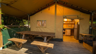 Terrasse en bois avec table de pique-nique devant Safari Lodge 1, vue sur cuisine rustique de la tente.