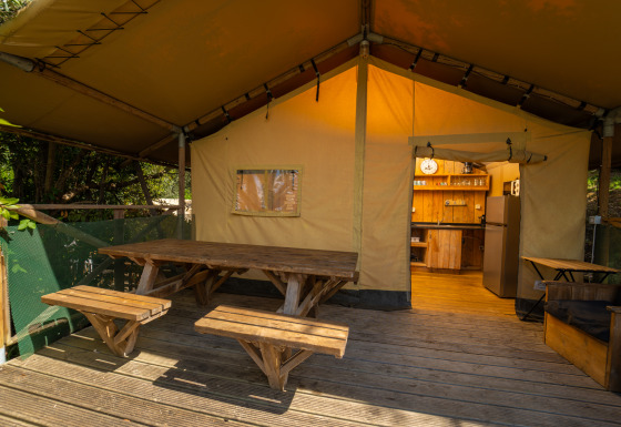 Terrasse en bois avec table de pique-nique devant Safari Lodge 1, vue sur cuisine rustique de la tente.
