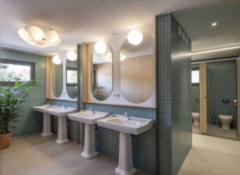 Moderne badkamer in een safaritent met vrijstaande wastafels, grote spiegels, planten en toilethokjes.