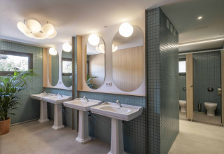 Bagno moderno in una tenda safari con lavandini a colonna, grandi specchi, piante e cabine WC private.