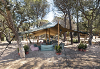 Udendørs loungeområde under stort telt i skovomgivelser på Wecamp Santa Cristina i Catalonien, Spanien.