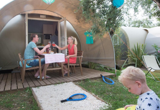 Gezin geniet van een maaltijd bij een Coco Suite safaritent, kind speelt op het gras in de zomer.