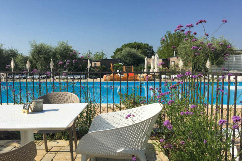 Outdoor dining area with white chairs and flowers overlooking pool at Vacanze Glamping Boutique in Lombardy.