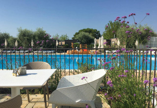Outdoor dining area with white chairs and flowers overlooking pool at Vacanze Glamping Boutique in Lombardy.