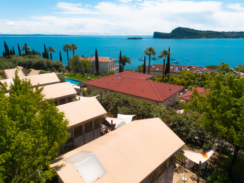 View of Vacanze Glamping Boutique in Lombardy, Italy, with tents, trees, and a stunning lake background.