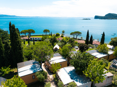 Aerial view of Vacanze Glamping Boutique featuring cabins, trees, and a lake view in Lombardy, Italy.