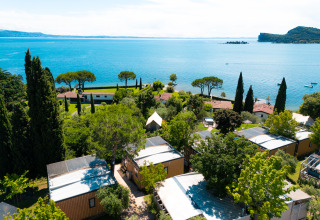 Aerial view of Vacanze Glamping Boutique featuring cabins, trees, and a lake view in Lombardy, Italy.
