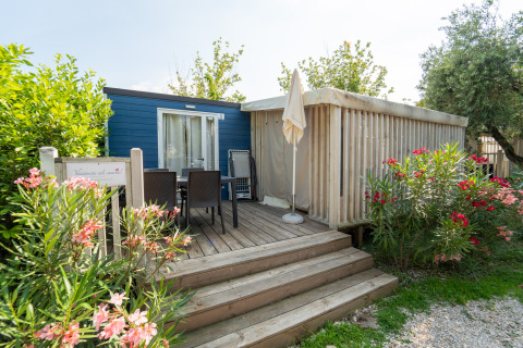 Outdoor terrace with seating and umbrella in front of Cottage Clever lodge, surrounded by lush plants.