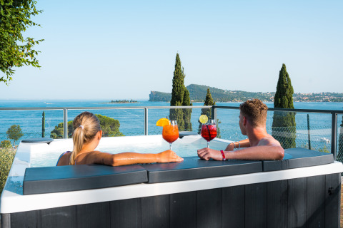 Couple relaxing in a hot tub with drinks, overlooking Lake Garda at Vacanze Glamping Boutique, Lombardy, Italy.