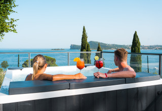 Couple relaxing in a hot tub with drinks, overlooking Lake Garda at Vacanze Glamping Boutique, Lombardy, Italy.