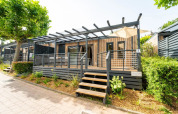 Modern lodge with a spacious front porch and wooden railing, surrounded by greenery on a sunny day.