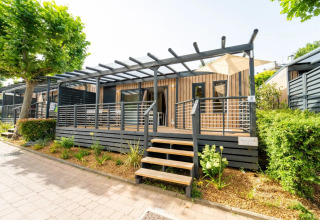 Lodge moderno con terraza amplia, barandilla de madera y vegetación alrededor, bajo el sol brillante.