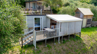 Lodge Cottage Clever avec terrasse en bois, perché sur une colline verdoyante entourée d’arbres.