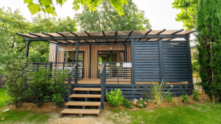 Exterior view of Cottage Next XL Superior Dog lodge with wooden terrace, steps, and lush greenery all around.