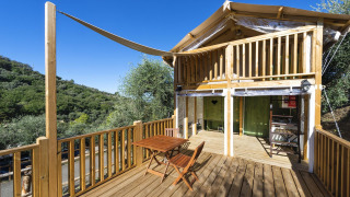 Tente safari Air Lodge avec terrasse en bois, coin repas extérieur et vue sur les collines verdoyantes environnantes.