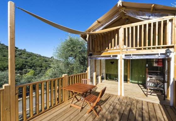 Safari tent Air Lodge met houten terras, tafeltje en stoelen, omgeven door groen en heuvelachtige natuur.