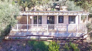 Vue avant du lodge Cottage Next L avec grande terrasse en bois, entouré d’arbres et de verdure