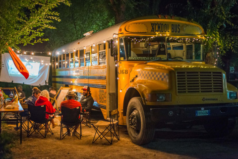 Ambiance chaleureuse près de la tiny house Schoolbus, soirée cinéma en plein air avec guirlandes lumineuses.