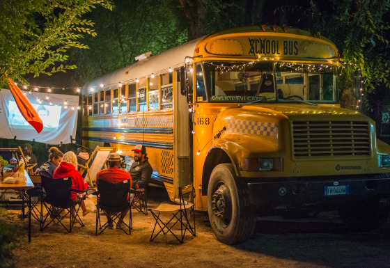 Ambiance chaleureuse près de la tiny house Schoolbus, soirée cinéma en plein air avec guirlandes lumineuses.